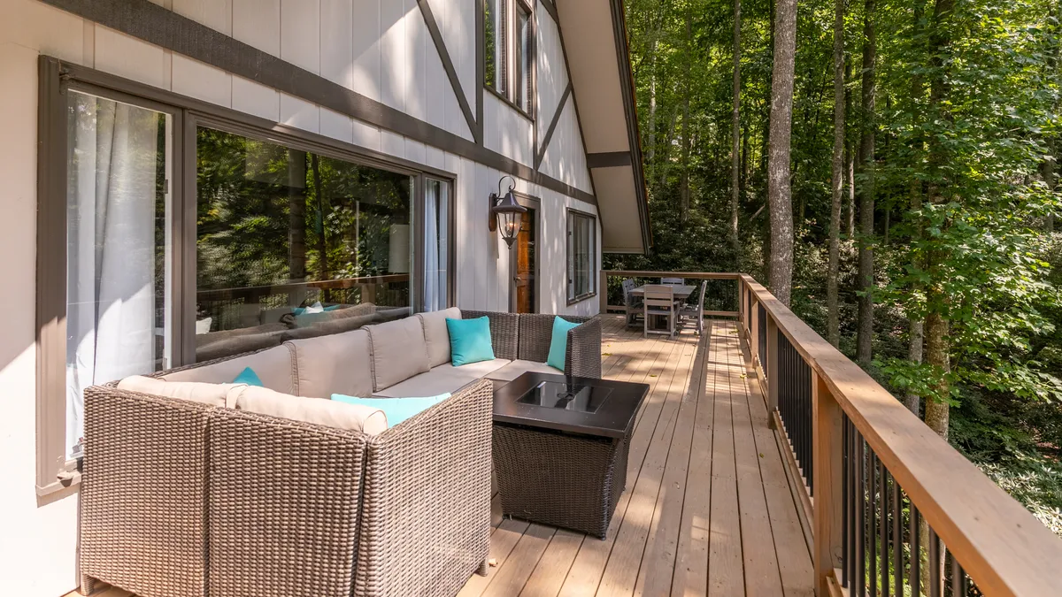 A tranquil exterior scene with an outdoor seating area on a wooden deck, nestled among mature trees. The peaceful setting suggests a private, natural environment that is both relaxing and safe for pets to explore and unwind.