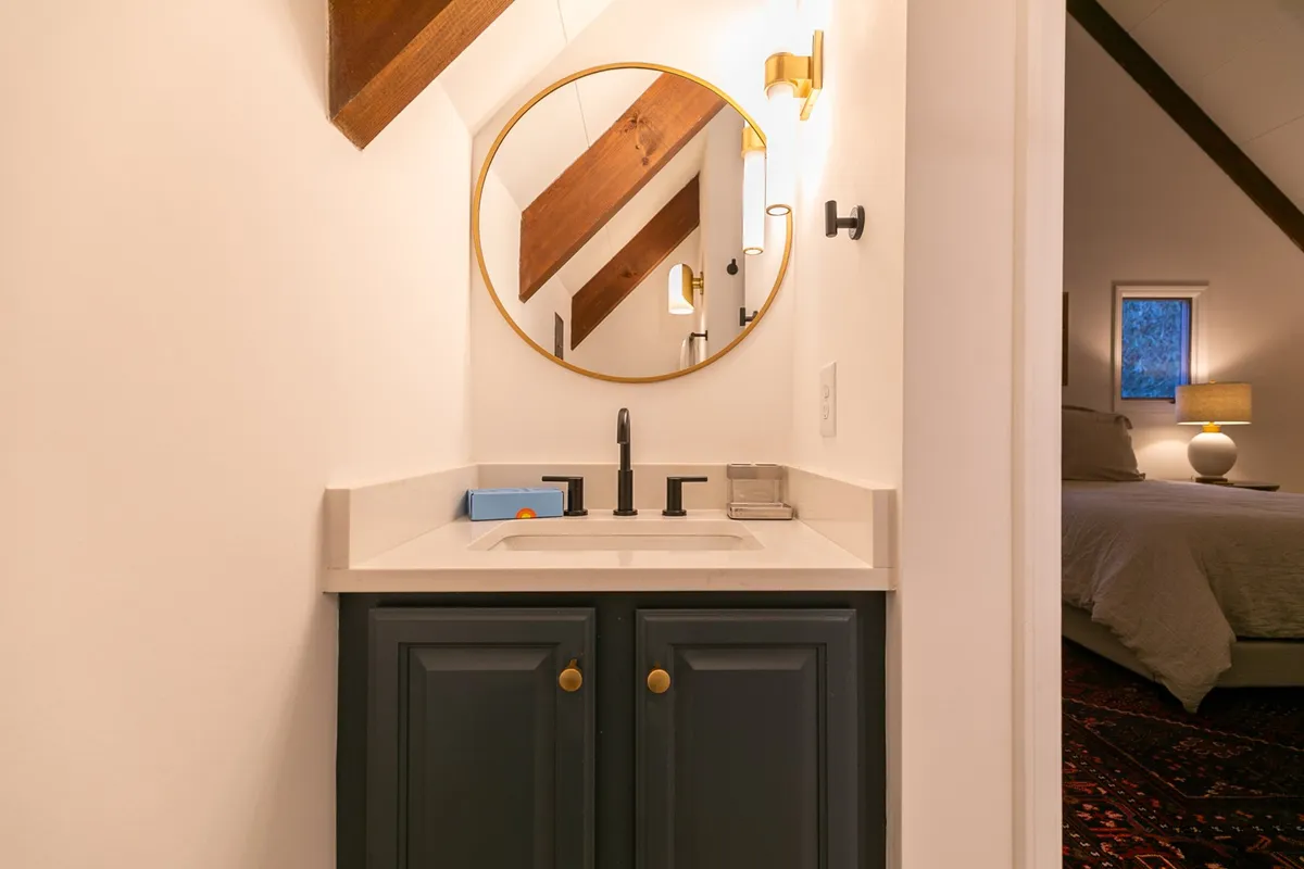 A calming ensuite bath accented by a stylish sink, mirror, and lighting fixtures, with rustic wooden beams overhead. The space exudes serenity and is perfect for unwinding during morning or evening routines.