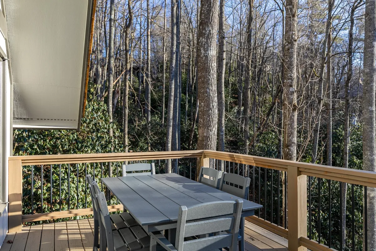This image presents a tranquil deck area with a table surrounded by trees, suggesting a space perfect for outdoor dining, morning coffee, or relaxed family gatherings. The lush greenery and filtered sunlight evoke the calm and privacy described in the narrative.