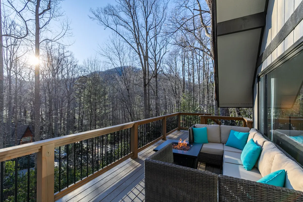 This exterior shot highlights an inviting outdoor seating area complete with a fire pit, set against a panoramic view of forest and mountains. The space is ideal for relaxing, socializing, and enjoying warm evenings around the fire.