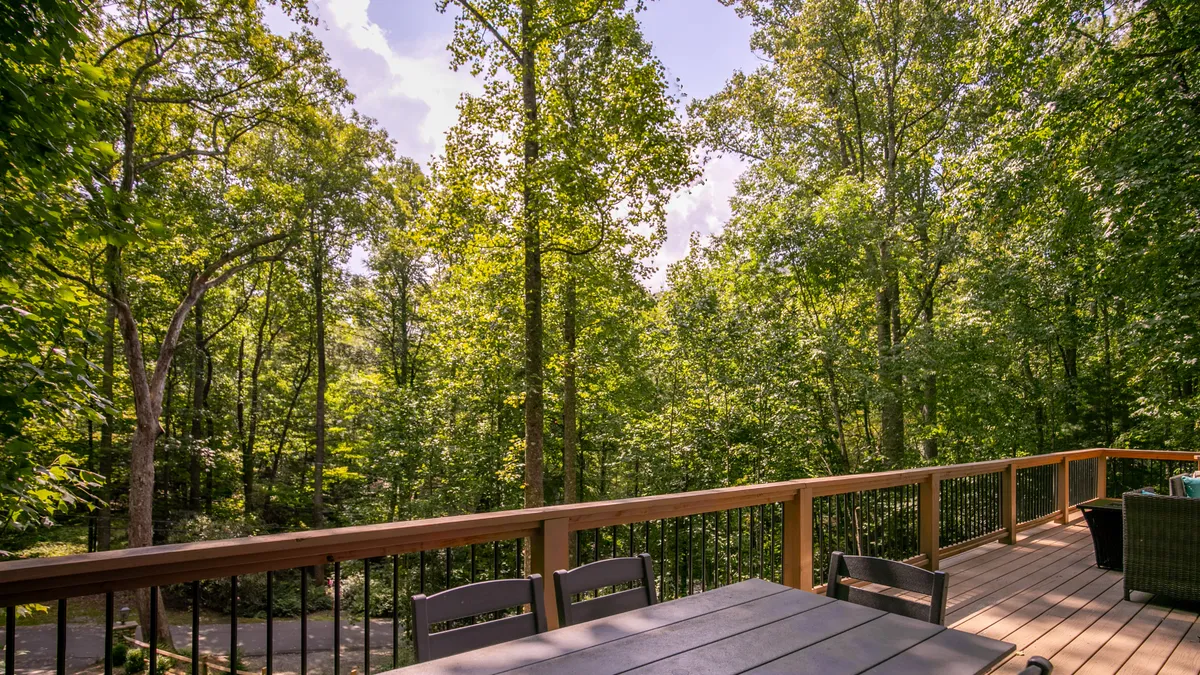 A tranquil outdoor deck surrounded by lush trees, featuring comfortable outdoor furniture perfect for relaxing after a hike or enjoying morning coffee. The natural wood and serene setting immerse the viewer in the mountain retreat experience.