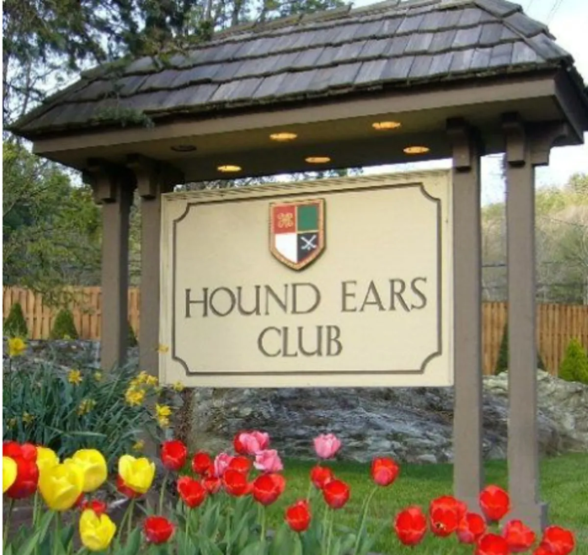 A cheerful exterior shot featuring the Hound Ears Club signage surrounded by colorful flower beds. The sense of community and well-maintained grounds creates a welcoming atmosphere for both guests and their pets.