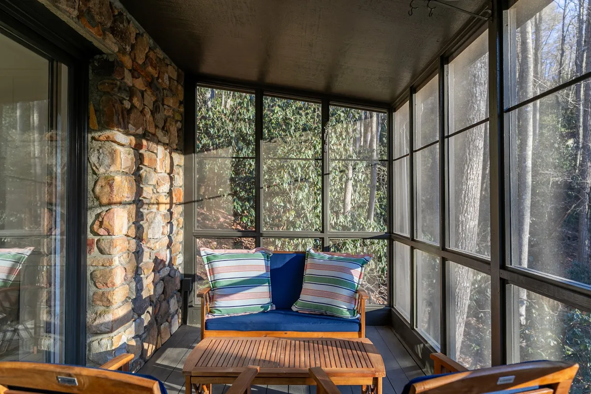 A welcoming sunroom with stone walls, striped cushions, and wooden furniture, set up for both relaxation and enjoying nature views. The bright, airy space is ideal for reading or spending quiet time, with a direct connection to the outdoors visible through windows.