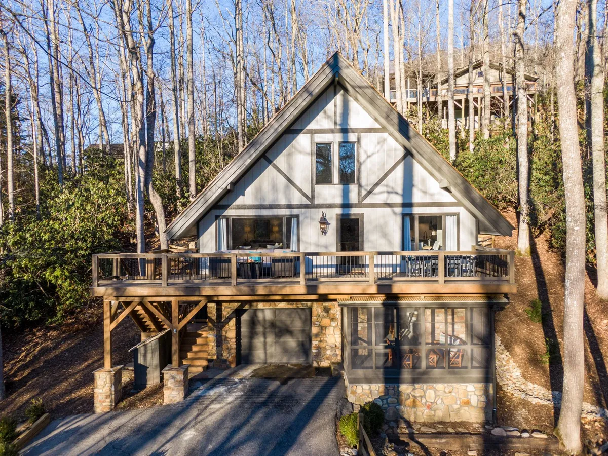 The image captures the A-frame structure's inviting wooden deck, with ample space for gatherings. The deck is surrounded by natural landscaping and offers a glimpse of the stone facade, providing a seamless connection between the home and the outdoors—ideal for alfresco dining and evening relaxation.